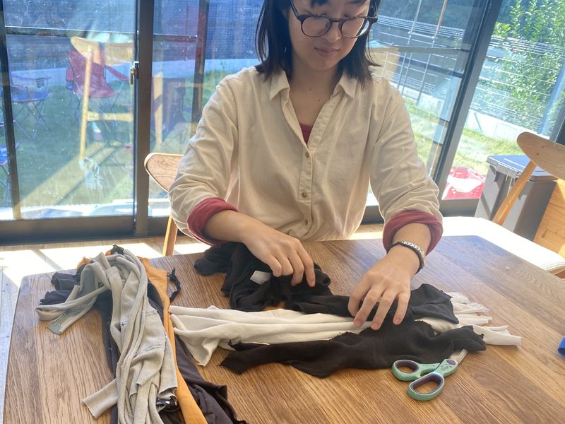 日の差す食卓で、女性がひとりで布を裂いて手仕事をしている写真